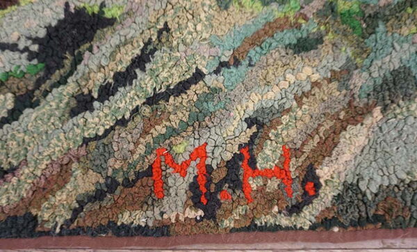 Chunky textured rug in greens, browns, and black with clearly visible red initials m. H.