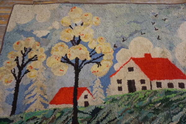 A textured shag rug with a pastoral scene of red houses, yellow trees, and a blue sky on wood floor.