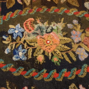 Hooked rug detail displays a bright floral medallion and a scrolling border on a dark green background.