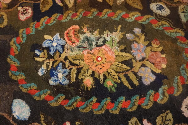 Hooked rug detail displays a bright floral medallion and a scrolling border on a dark green background.