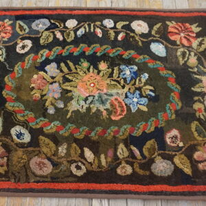 Dark floral rug with a colorful center medallion, thick texture, and a red inner border on wood flooring.