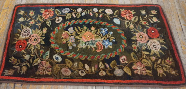 Dark floral rug with a colorful center medallion, thick texture, and a red inner border on wood flooring.