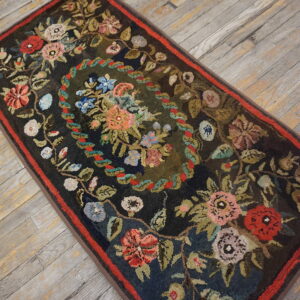 Textured dark runner rug featuring an oval floral garland and a red border on distressed wood flooring.