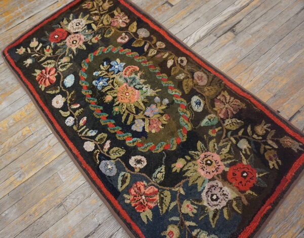 Textured dark runner rug featuring an oval floral garland and a red border on distressed wood flooring.