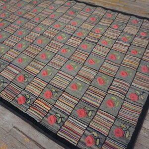 Gray and multicolored checkered rug with pink floral motifs and a black border on distressed wood floor.