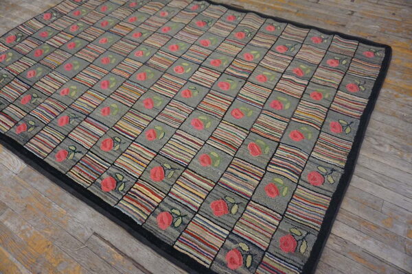 Gray and multicolored checkered rug with pink floral motifs and a black border on distressed wood floor.