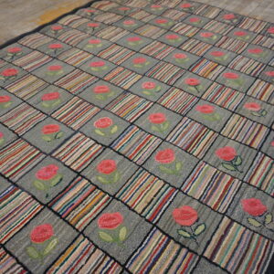 Gray and multicolored checkered rug with pink rose motifs displayed on rustic wood flooring.