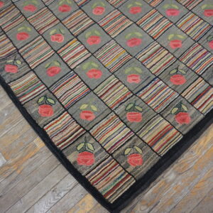 Black-bordered hooked rug with diagonal blocks of gray florals and multicolored stripes on wood flooring.
