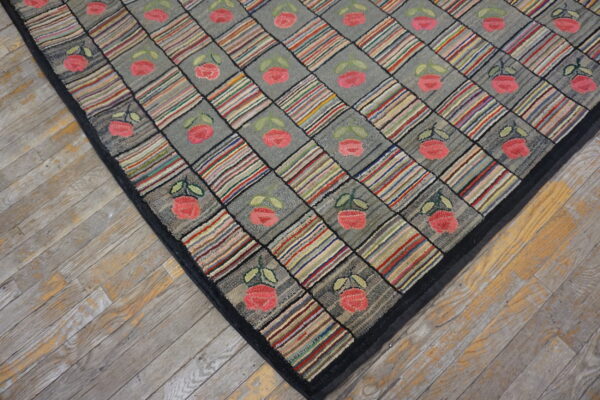 Black-bordered hooked rug with diagonal blocks of gray florals and multicolored stripes on wood flooring.