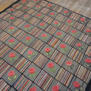 Hooked rug featuring a multicolored striped and rose checkerboard pattern on weathered wood floors.