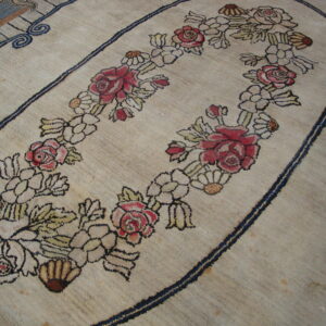 A close-up of a textured beige rug features a red and pink floral oval design outlined in dark navy blue.