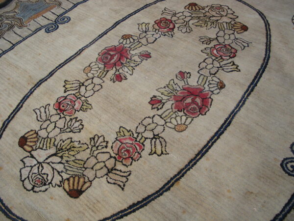 A close-up of a textured beige rug features a red and pink floral oval design outlined in dark navy blue.