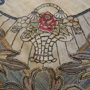 A highly textured rug displays a central floral design with a red rose and surrounding blue and brown scrollwork.