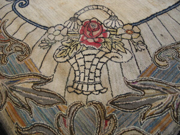 A highly textured rug displays a central floral design with a red rose and surrounding blue and brown scrollwork.