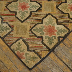 Close-up of a hooked rug with beige floral patterns and multicolored stripes on worn wood floors.