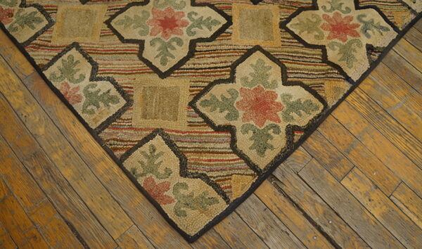 Close-up of a hooked rug with beige floral patterns and multicolored stripes on worn wood floors.