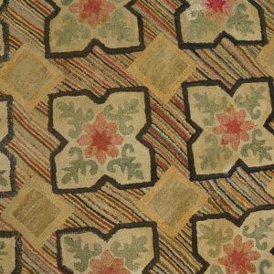 Close view of a hooked rug with beige floral quatrefoils against a multi-striped background on wood flooring.