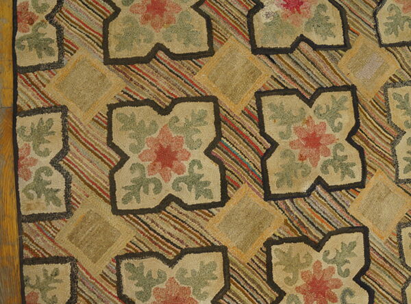 Close view of a hooked rug with beige floral quatrefoils against a multi-striped background on wood flooring.