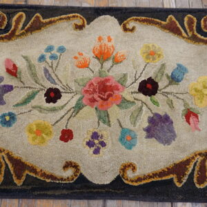 Textured rug with a colorful floral bouquet and dark scrolled border, lying on weathered wood planks.