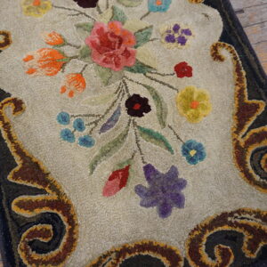 Ornate hooked rug featuring a colorful floral bouquet and scrollwork border on distressed wooden floors.