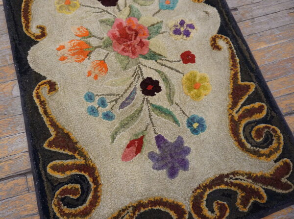 Ornate hooked rug featuring a colorful floral bouquet and scrollwork border on distressed wooden floors.