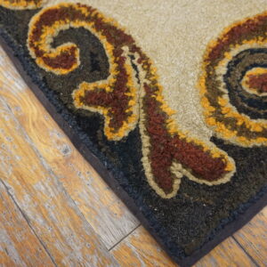 Textured rug corner showing beige, rust, and gold scrollwork on a dark field over distressed wood planks.