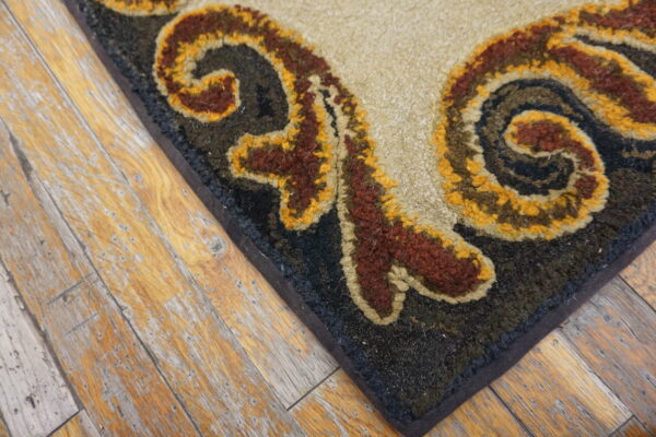 Textured rug corner showing beige, rust, and gold scrollwork on a dark field over distressed wood planks.