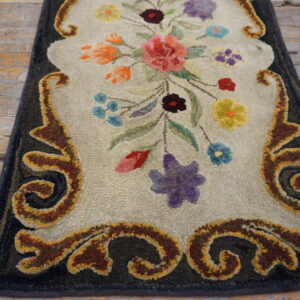 Beige, multi-colored floral rug with a dark border and sculpted scrollwork lays on worn wooden planks.