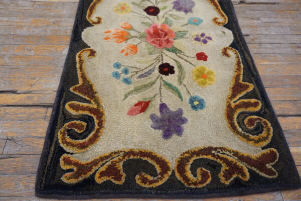 Beige, multi-colored floral rug with a dark border and sculpted scrollwork lays on worn wooden planks.