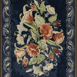Textured navy blue rug displaying a floral medallion of rust, cream, and green, framed by a scrolled light border.