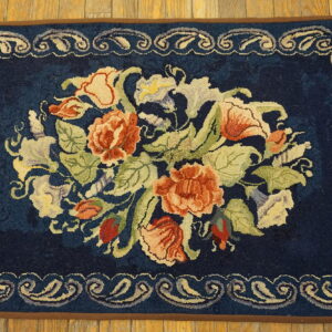 Navy rug with a central floral bouquet in peach, green, and cream, featuring a scrolling border on wood floors.