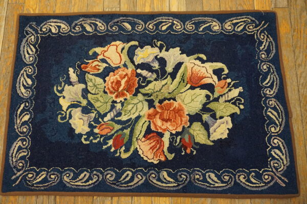 Navy rug with a central floral bouquet in peach, green, and cream, featuring a scrolling border on wood floors.