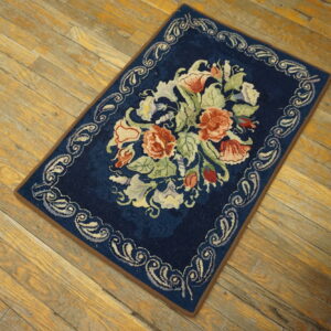 Navy blue rug with a large multicolored floral bouquet and scrolling border on wood planks.