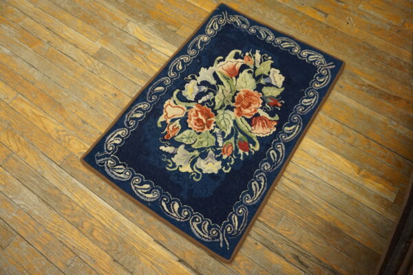 Navy blue rug with a large multicolored floral bouquet and scrolling border on wood planks.