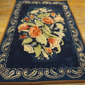 Dark blue rug with peach and green florals and an ornate border resting on light wood floors.