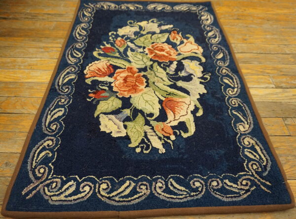 Dark blue rug with peach and green florals and an ornate border resting on light wood floors.
