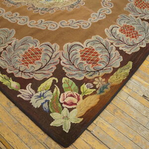 Textured brown rug corner with gray ornate motifs and colorful low-pile flowers, set on distressed wood flooring.