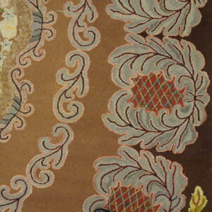 Brown patterned rug with hooked floral and scrolled motifs lies next to distressed light wood flooring.