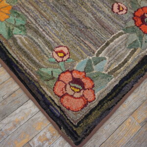 Hooked rug corner with orange and pink floral motifs resting on distressed gray wood plank flooring.