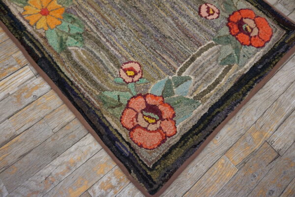 Hooked rug corner with orange and pink floral motifs resting on distressed gray wood plank flooring.