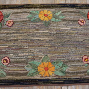 Floral-bordered rug with a textured, multicolored striped field resting on rustic wooden flooring.