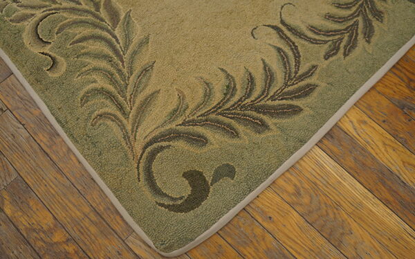 Close-up of a green hooked rug with a scrolling leafy pattern resting on distressed wood planks.