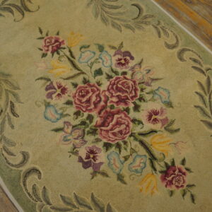 Sage green floral rug featuring a dense bouquet of maroon, purple, and yellow flowers on wood flooring.