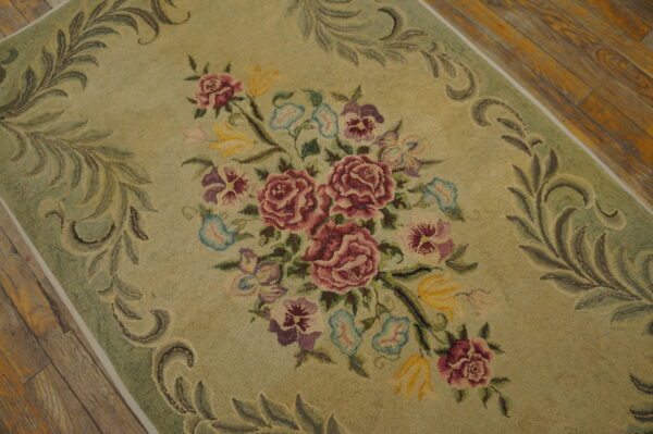 Sage green floral rug featuring a dense bouquet of maroon, purple, and yellow flowers on wood flooring.