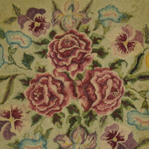 Hooked rug detail displaying pink roses, purple pansies, and yellow flowers against a light green textured ground.