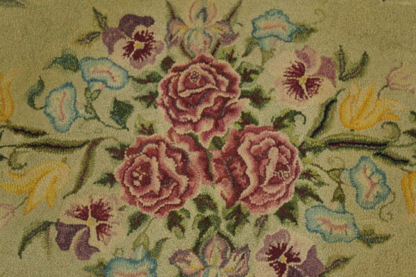 Hooked rug detail displaying pink roses, purple pansies, and yellow flowers against a light green textured ground.