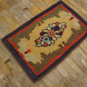 Multicolored looped rug featuring a floral bouquet on a gold background is placed on weathered wood planks.