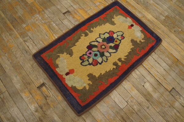 Multicolored looped rug featuring a floral bouquet on a gold background is placed on weathered wood planks.