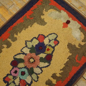 Looped pile rug featuring a multicolored floral medallion on a gold field, placed on distressed wood flooring.