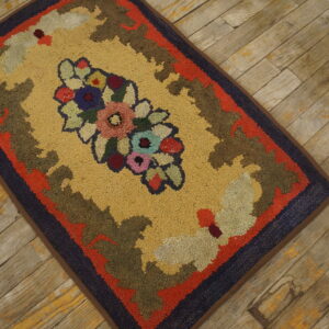 Gold hooked rug featuring a brightly colored floral cluster and multi-toned borders on rustic wood.